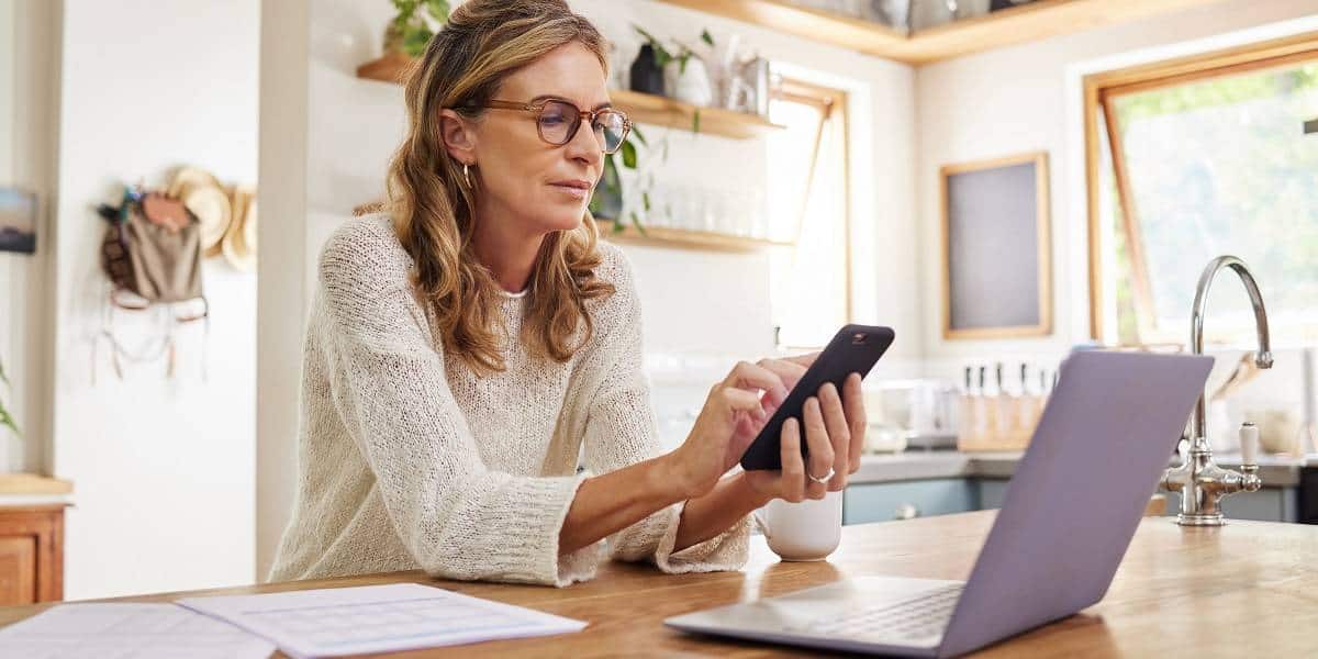 Woman with laptop and phone in home kitchen managing finances event
