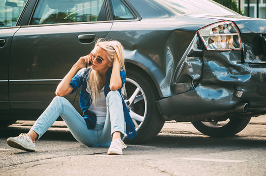 woman in front of wrecked car on phone