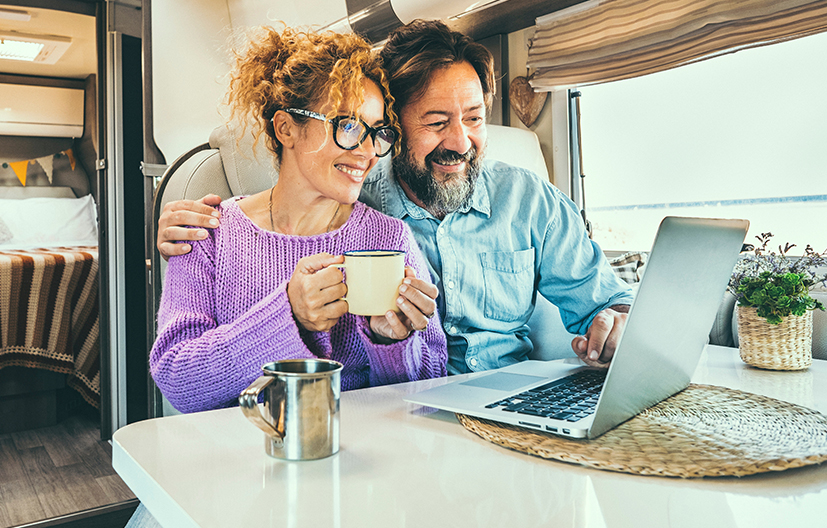 couple in RV looking at computer while drinking coffee