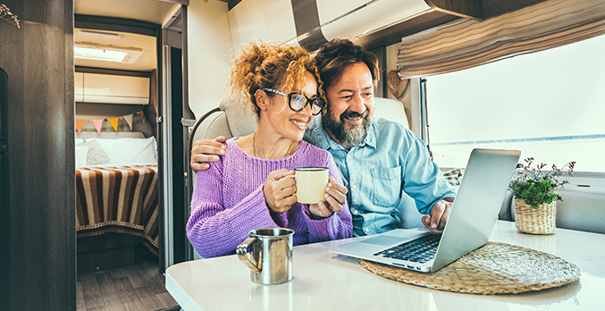 couple in RV looking at computer while drinking coffee